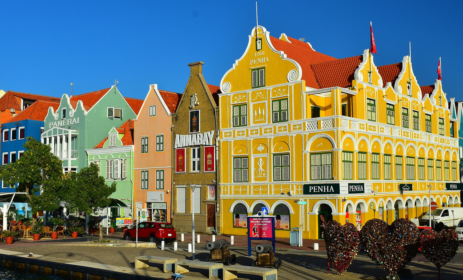 The colorful buildings of Handelskade street in downtown Willemstad.The buildings featured dutch architecture and from left to right are cobalt blue, mint green, lime green, peach, exposed brown brick, and marigold yellow.