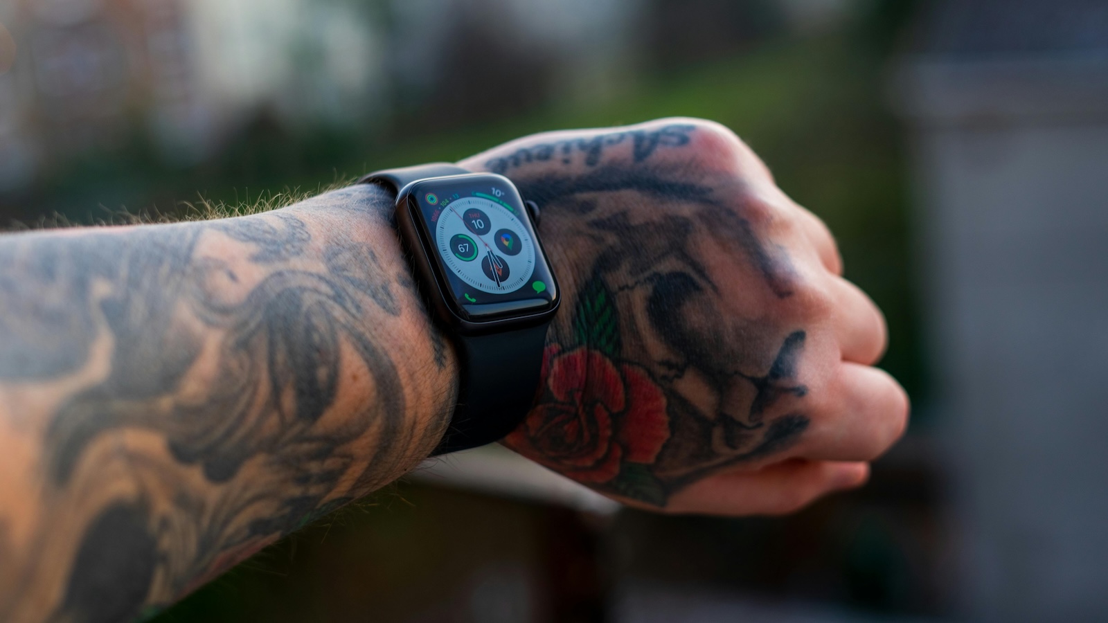 An Apple Watch on a man's wrist. His forearm and hand are heavily tattooed.