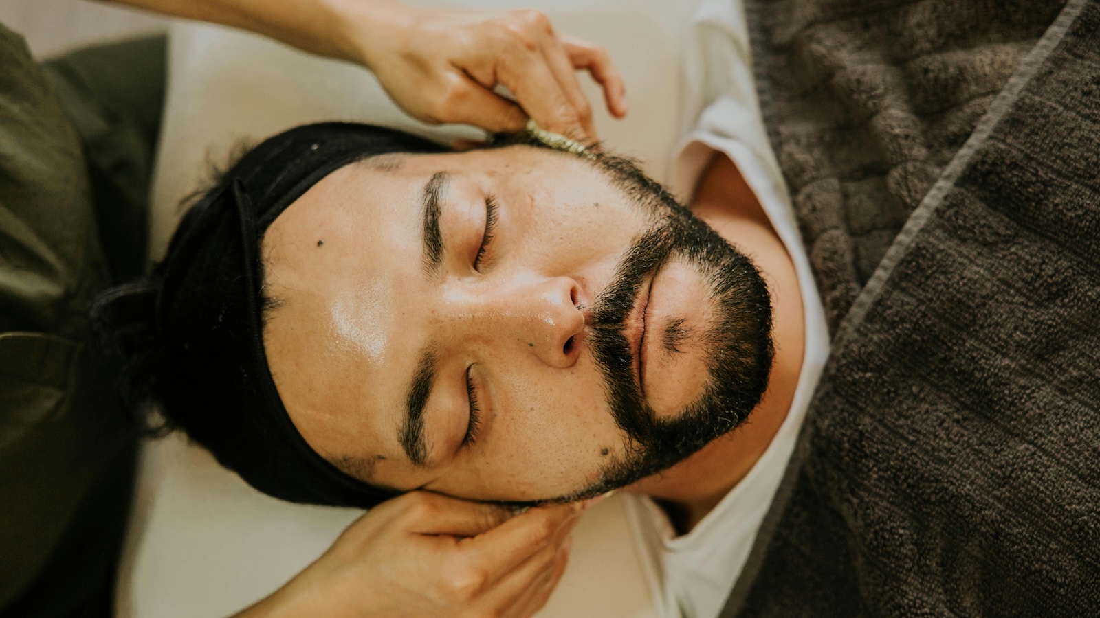 Man receiving professional facial treatment at a day spa, eyes closed, calm and relaxed. Clean, descriptive, accessible. Good boy for thinking about that too.