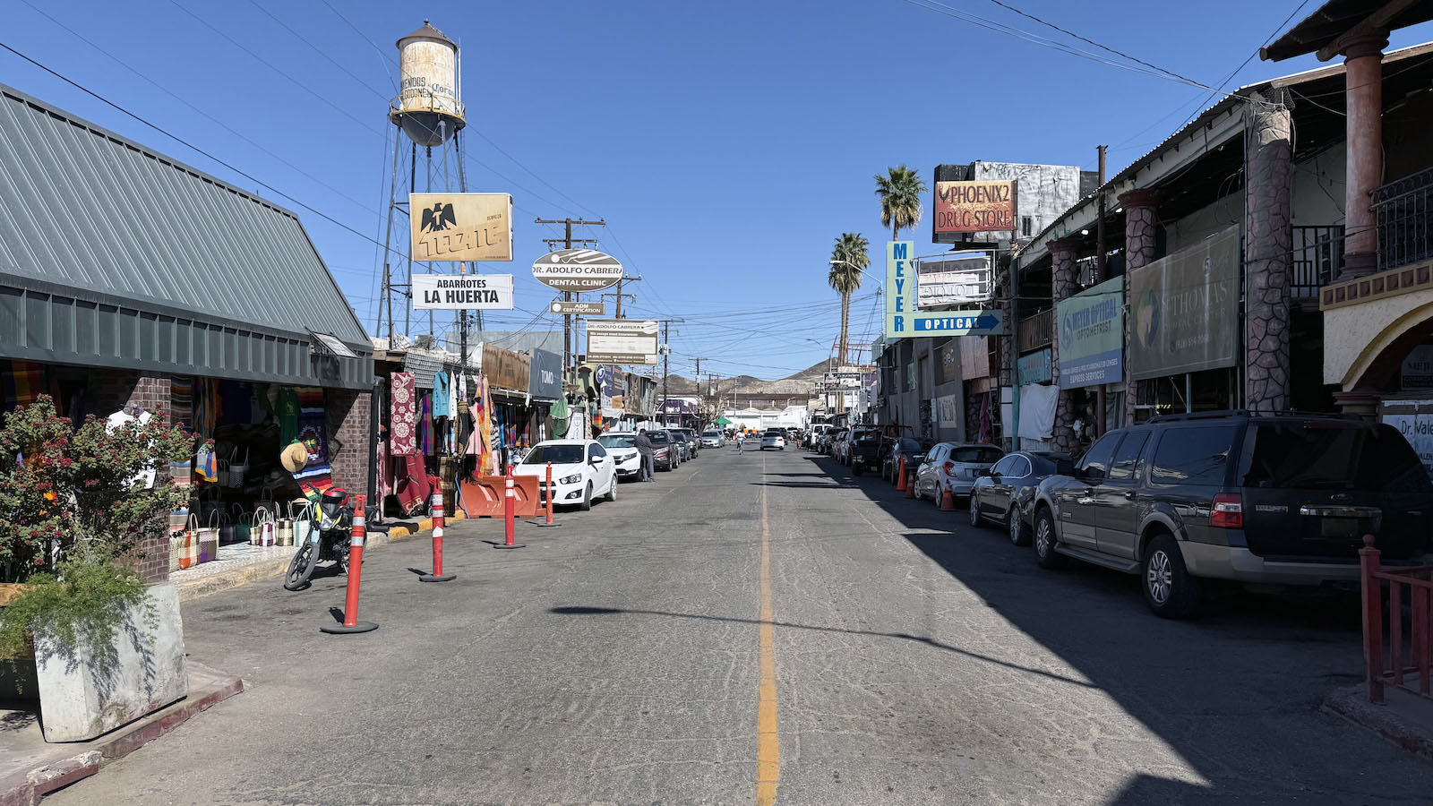 A view of 2nd Street in Los Algodones facing north towards the border. There are signs for several dental clinics, opticians, and pharmacies.