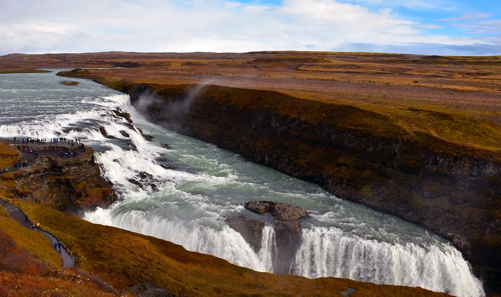 reykjavik A view of the double-tiered waterfall Gullfoss taken from above, beneath a blue sky with fluffy white clouds.