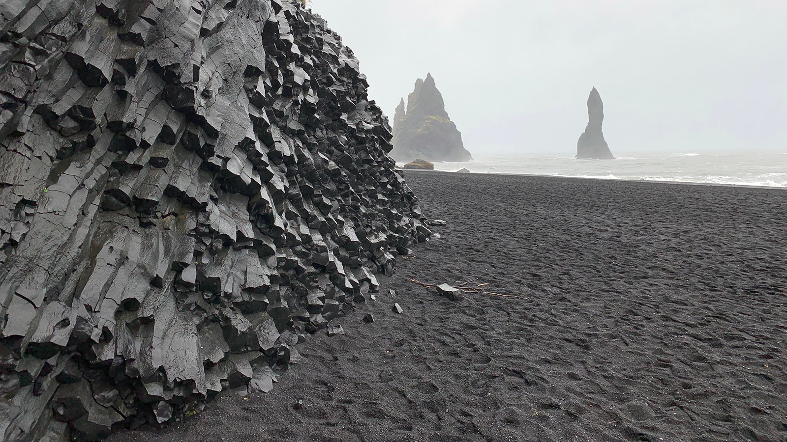 Reynisfjara A view of the black hexagonal basalt formations and black sand beach of Reynisfjara. In the distance, you can see the water's edge of the Atlantic and rock spires rising from the ocean.