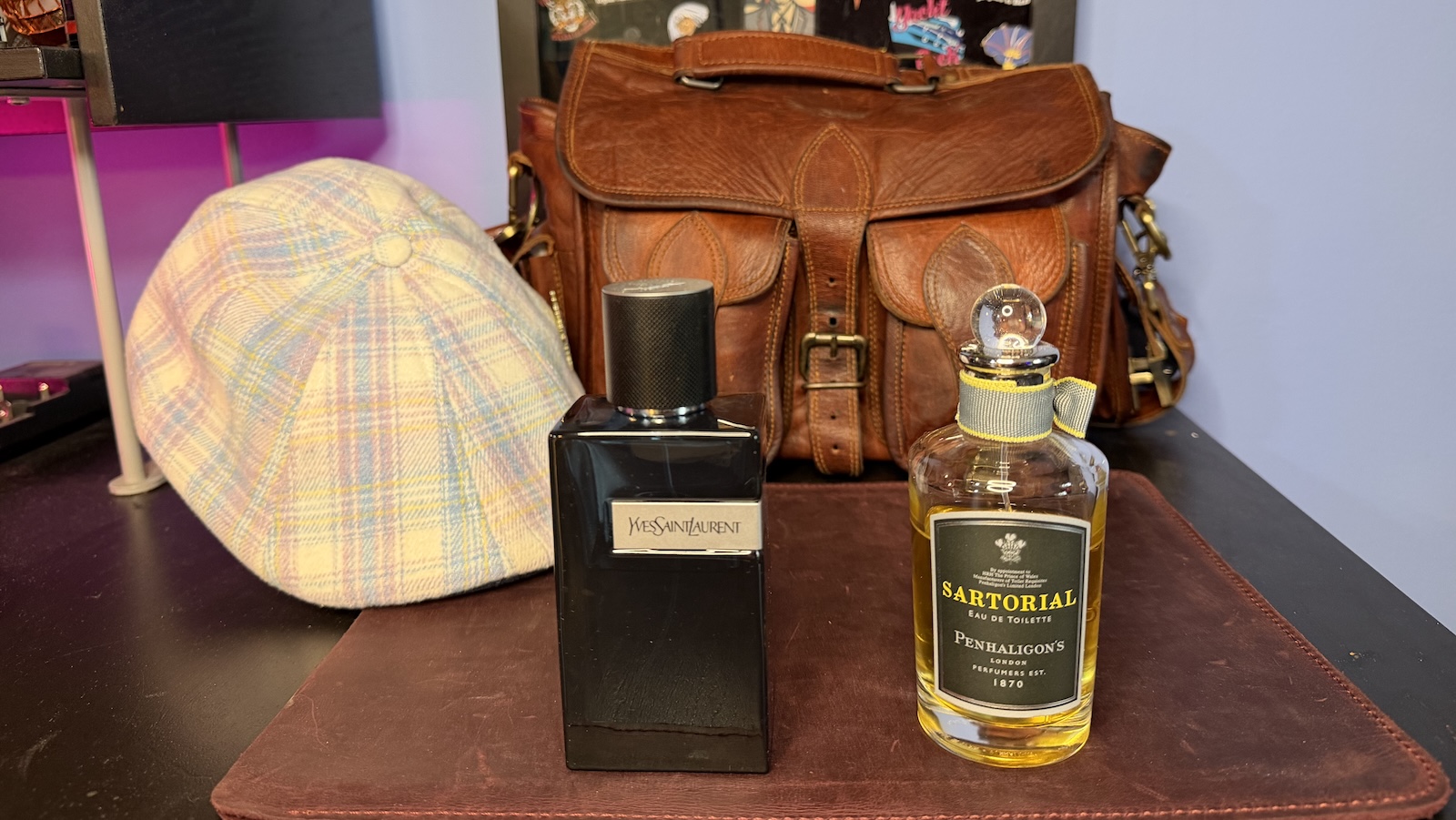 Spring-Scents Yves Sait Lauren Y and Penhaligon's Sartioal sitting on a leather mat, a Boston Scally Cottontail Scally Cap and leather messenger bag are visible in the background.