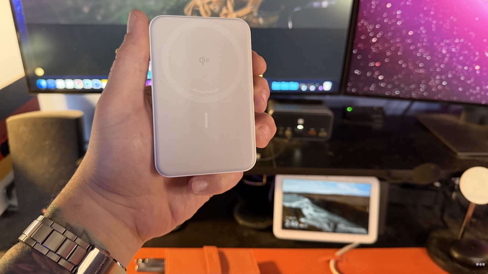 My hand holding the Mii Bluetooth 5.3 Transmitter Receiver Anker MagGo 10K Power Bank, my office desk with my displays can be seen in the background.
