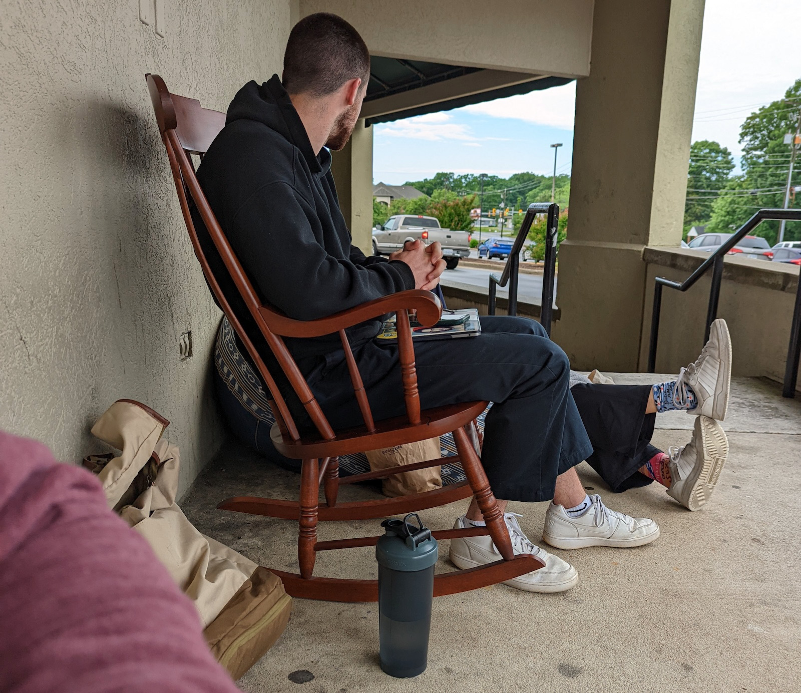A man sitting in line at the tattoo parlor in a wooden rocking chair.