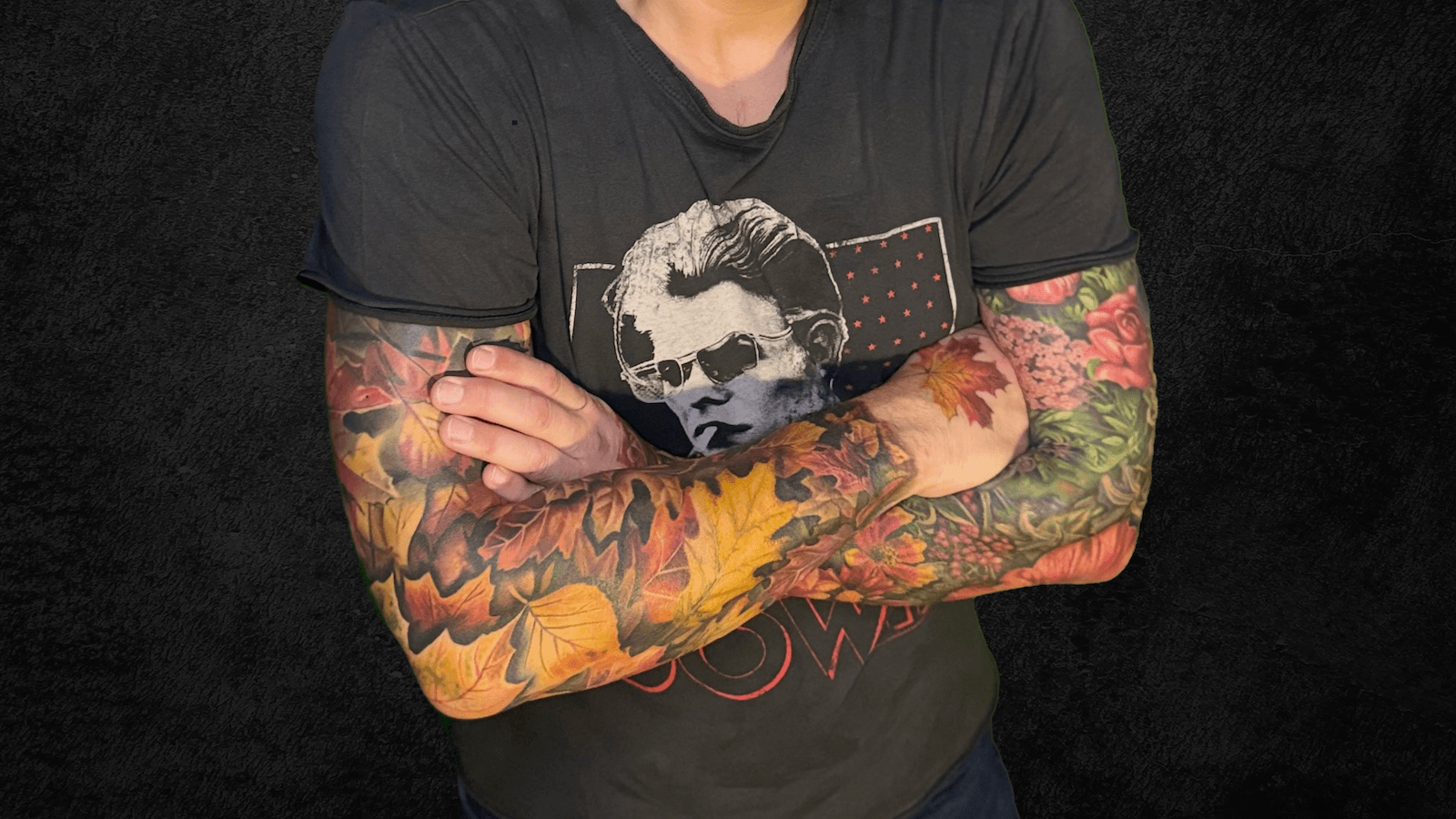 My folded arms with completed tattoo sleeves. My right arm is covered in autumn leaves; my left arm is covered in flowers.