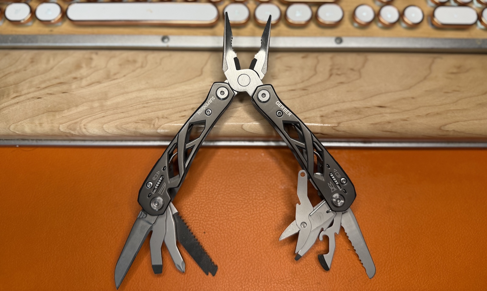 gerber-suspension The Gerber Suspension multi-tool is lying on an orange leather background and a pale wood keyboard rest.