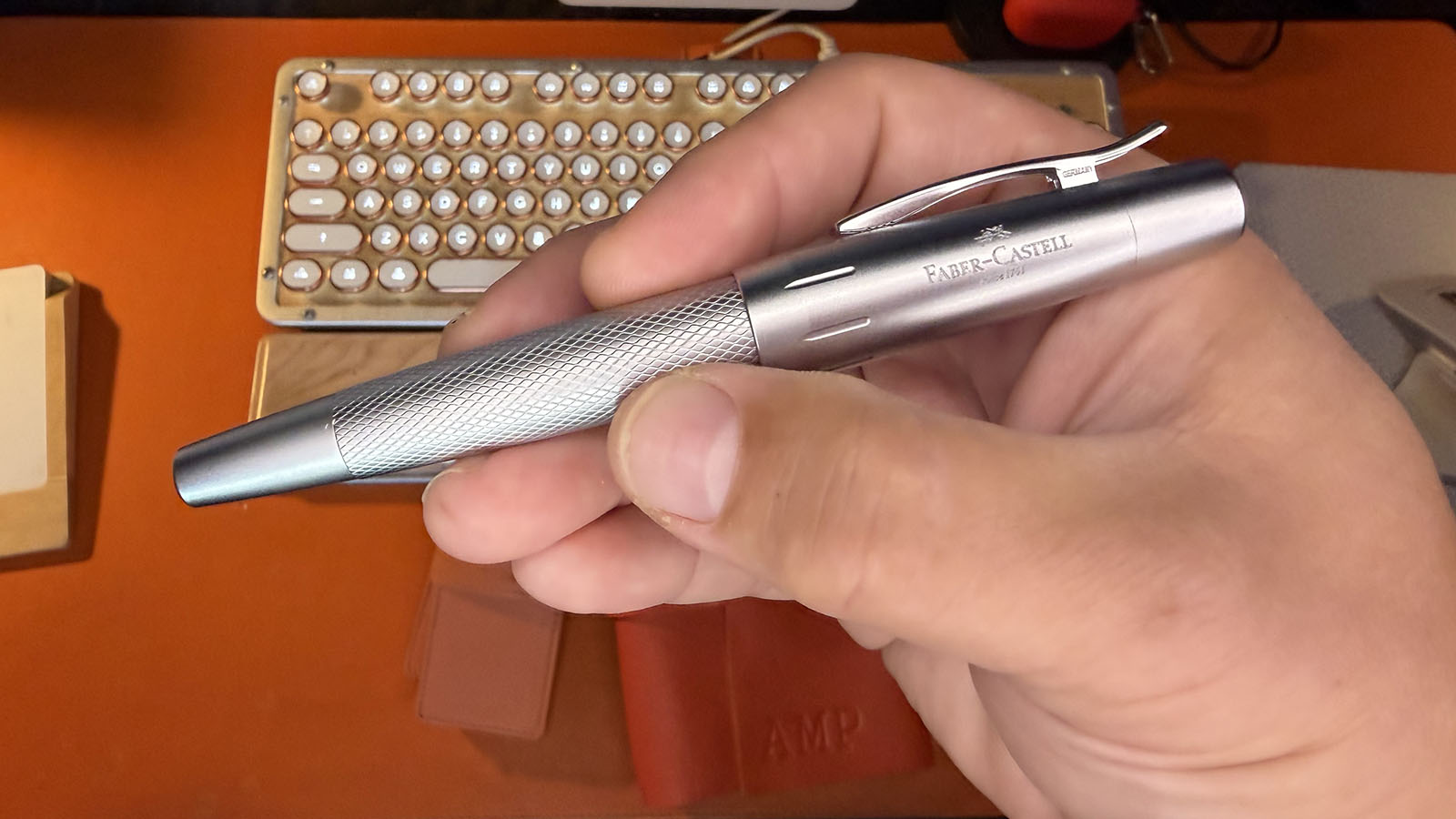 Close-up of a capped Faber-Castell e-motion fountain pen held in one hand, showing its diamond-patterned silver barrel, matte metal cap and curved pocket clip.