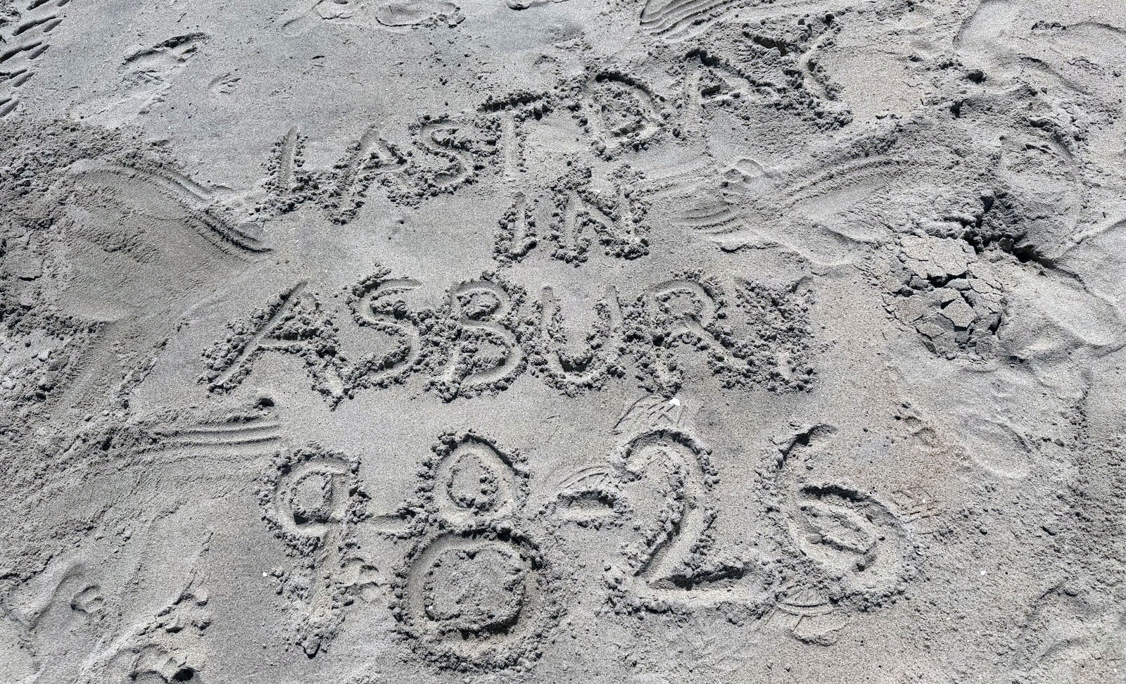 last-day-in-asbury “Last day in Asbury 9/8/2026" written in the sand with footprints around it.