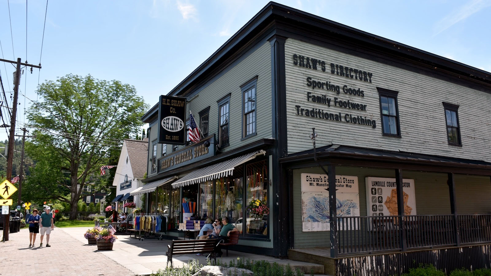 Shaw’s General Store on Main Street in Stowe, with clothing displays, benches, flowers, and pedestrians outside.