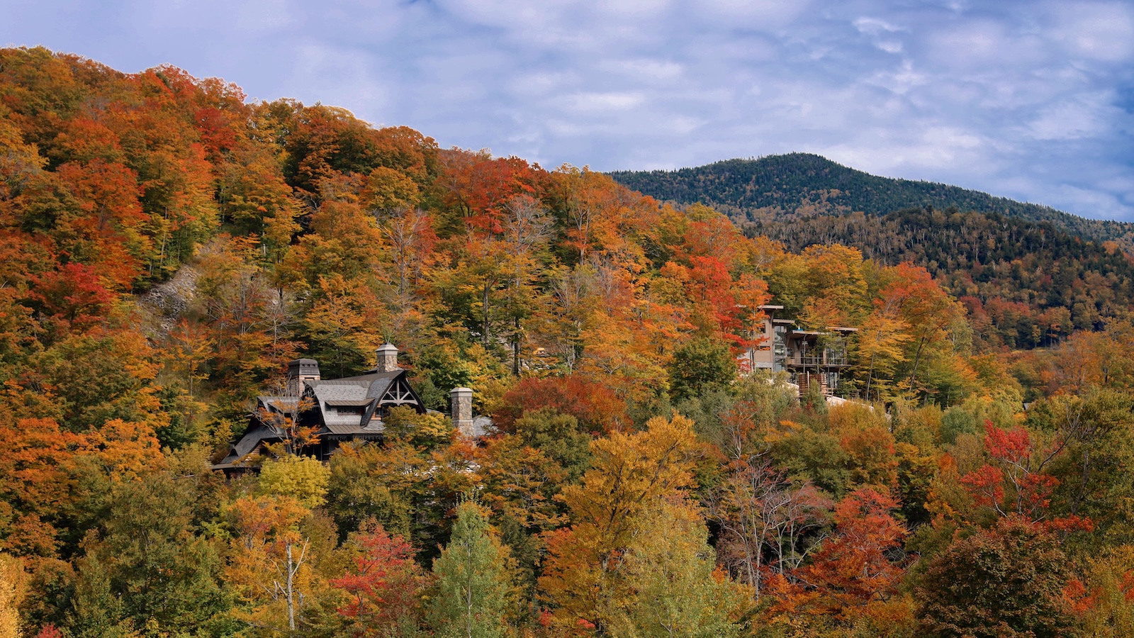 Vermont mountainside covered in vivid orange, red, yellow, and green autumn foliage with homes nestled among the trees.